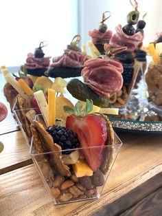 several snacks are arranged in clear containers on a wooden table with fruit and crackers