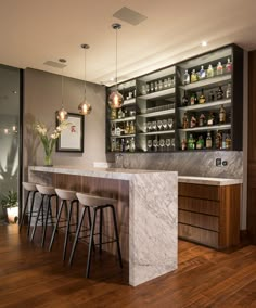 a kitchen with marble counter tops and bar stools in front of shelves filled with liquor bottles