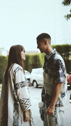 a man and woman standing next to each other in front of a parking lot with cars