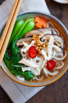 a bowl filled with noodles and vegetables next to chopsticks on top of a napkin