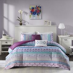 a bed with purple and blue comforters in a bedroom next to a white dresser