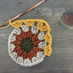 a crocheted dishcloth with an orange and white flower on it, next to a knitting needle