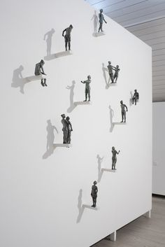 several small figurines are placed on the side of a white wall in an art gallery