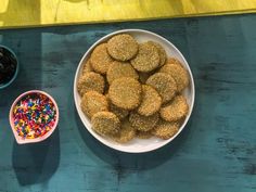 a white bowl filled with sprinkles next to a pink bowl full of cookies