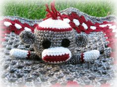 a crocheted sock monkey laying on top of a red and gray blanket in the grass