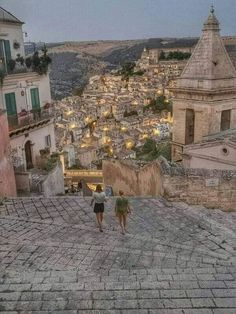 two people are walking up the stairs in an old town at night with lights on