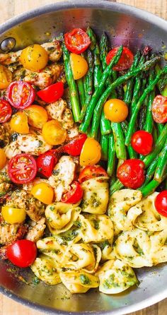 a pan filled with pasta, asparagus and tomatoes