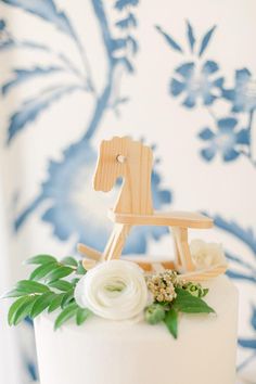 a small wooden rocking horse on top of a white cake with flowers and greenery