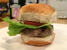 a hamburger with lettuce and tomato on a white plate in front of a counter