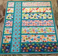 a quilted table runner made with colorful strips and fish on the border, sitting on top of a floral fabric