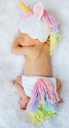 a baby wearing a crochet unicorn hat and diaper is sleeping on a fluffy white blanket