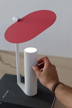 a hand is holding a red and white object on top of a black book next to a lamp