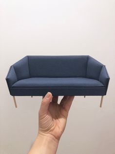 a person holding up a miniature couch in front of a white wall with no one on it