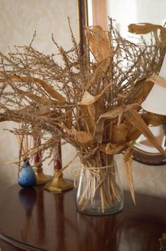 a vase filled with dried plants sitting on top of a wooden table next to a mirror