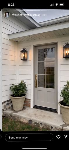 a white house with two large planters on the front porch and one door open