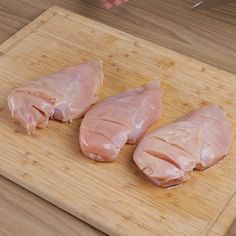 three pieces of chicken sitting on top of a wooden cutting board