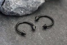 two pairs of black nose rings sitting next to each other on top of a rock