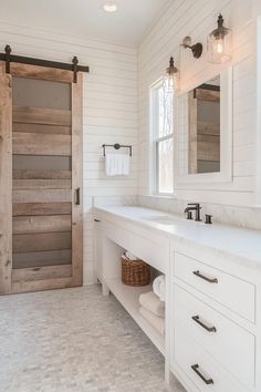 a bathroom with two sinks and a barn door in the middle of it, surrounded by white wood paneling