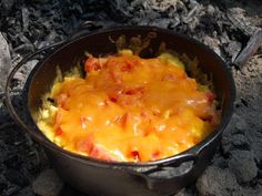 a casserole with cheese and tomatoes in a black pan on the ground next to some rocks