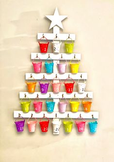 a christmas tree made out of cups hanging from hooks on the side of a wall