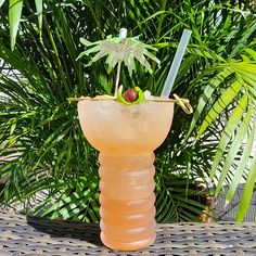 a tall glass sitting on top of a table next to palm trees and plants in the background