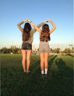 two girls are standing in the grass with their hands on their hipss and looking into the distance