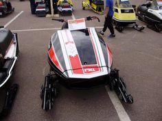 a red and white snowmobile parked in a parking lot next to other vehicles on the ground