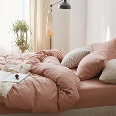 an unmade bed with pink sheets and pillows in a white room next to a window