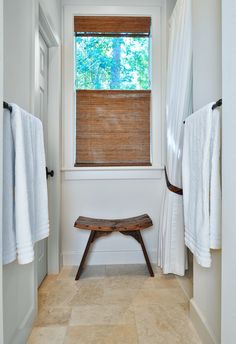 a wooden bench sitting under a window next to a white towel rack and shower curtain