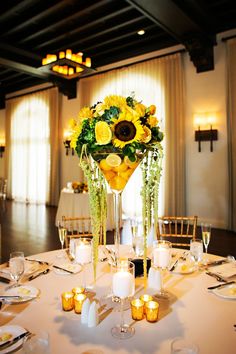 a centerpiece with sunflowers and greenery sits on a table at a wedding reception