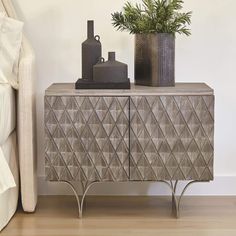 a sideboard with two vases on it next to a bed and a plant