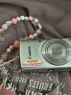 a camera sitting on top of a bed next to a beaded bracelet and necklace