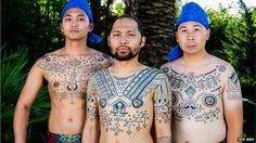 three men with tattoos on their chests standing next to each other in front of trees