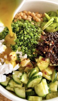 a white bowl filled with cucumbers, beans and other foodstuffs being drizzled over them