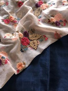 an embroidered blanket with flowers on it laying on top of a blue bed coverlet