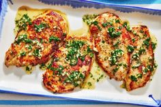 three pieces of chicken covered in sauce and parsley on a white plate with blue trim