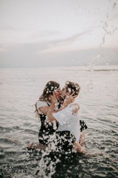 two people are kissing in the water with their arms around each other and splashing on them