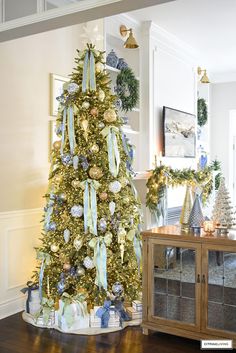 a decorated christmas tree with blue and gold ornaments in a living room area, surrounded by other holiday decorations