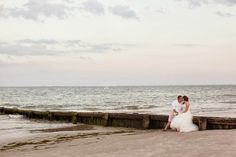 a bride and groom sitting on a pier by the ocean