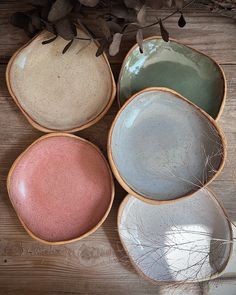 four different colored bowls sitting on top of a wooden table next to dried flowers and branches