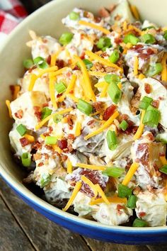 a bowl full of potato salad with cheese and green onions in it on a wooden table