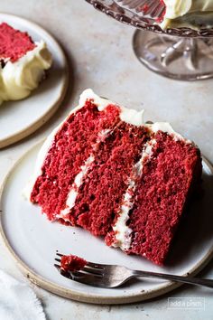 a slice of red velvet cake with white frosting on two plates next to a fork