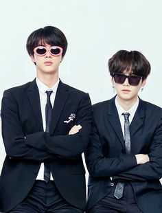 two men in suits and sunglasses standing next to each other with their arms crossed,