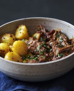 a bowl filled with meat and potatoes on top of a blue napkin next to a fork