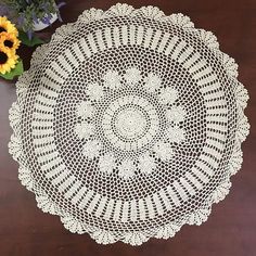 a crocheted doily sits on a table next to a vase with sunflowers