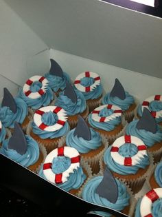 cupcakes decorated with blue frosting and shark fin shapes are in a box