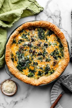 a quiche with spinach and cheese in a pie pan on a marble table