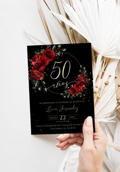 a woman holding up a black and red 50th birthday party card with flowers on it