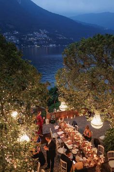 an outdoor dining area overlooking the water at night with lights on trees and people eating