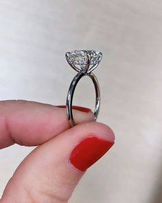 a woman's hand holding an engagement ring with two diamonds on it and red nail polish